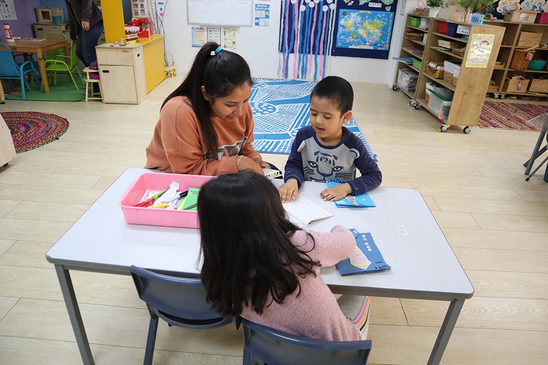 A caring educator supporting children with creative activities at a trusted early learning centre.